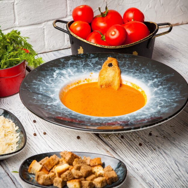 Zupa pomidorowa ze świeżymi pomidorami, zieleniami i serem na stole