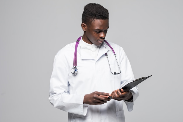 Bezpłatne zdjęcie Życzliwa afroamerykańska lekarka trzyma schowek i ono uśmiecha się przy kamerą odizolowywającą na szarym tle