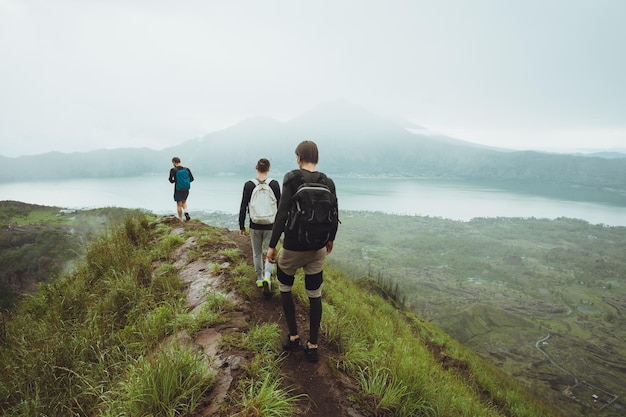 3 hombres caminan por la colina con mochilas y con nubes blancas y pico de volcán en el fondo