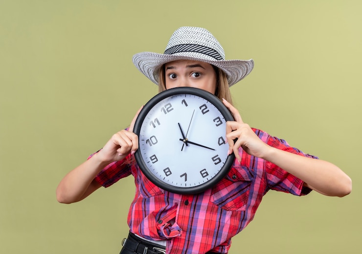 Photo Gratis a surprised lovely young woman in a checked shirt wearing hat holding wall clock