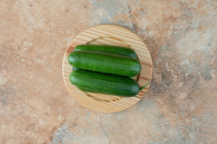 Photo Gratis a wooden plate with fresh cucumbers on marble table.