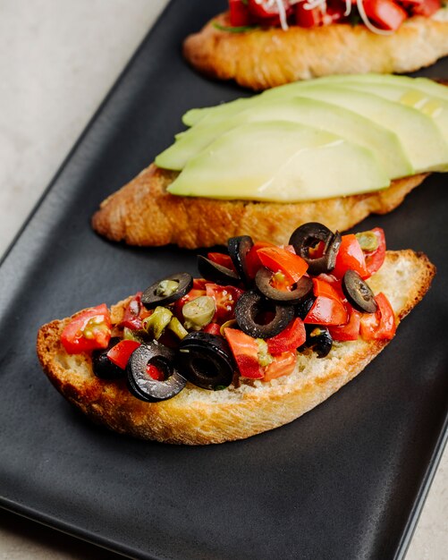 Abra los emparedados con las aceitunas y los tomates de la manzana dentro del plato negro.