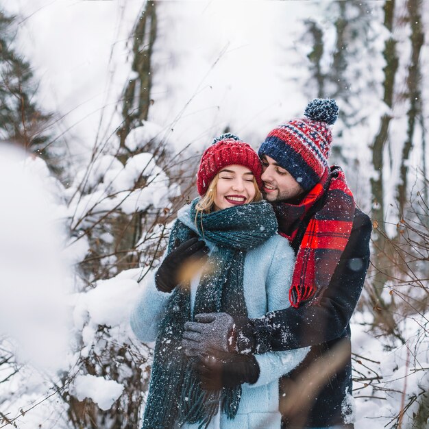 Abrazando a feliz pareja en el bosque de invierno