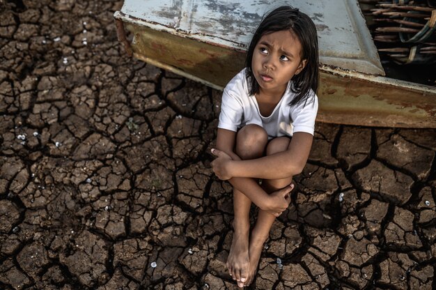 Abrazando sus rodillas y mirando al cielo en tierra seca, hay barcos de pesca, el calentamiento global.