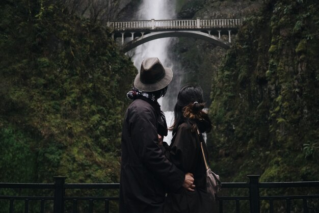 Abrazo de pareja asiática se encuentra ante una hermosa cascada en las montañas