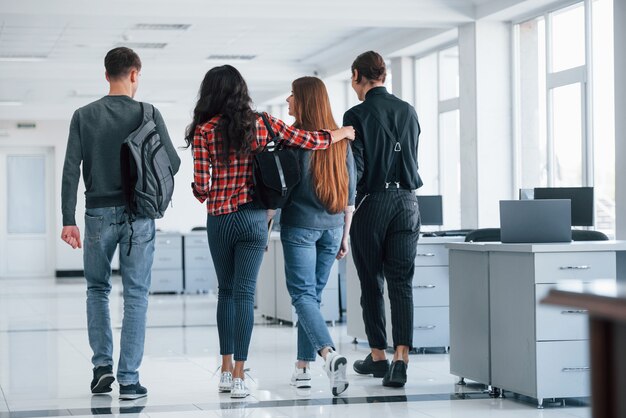 Abrazos amistosos. Grupo de jóvenes caminando en la oficina en su tiempo de descanso