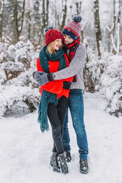 Abrazos elegante pareja en el parque cubierto de nieve