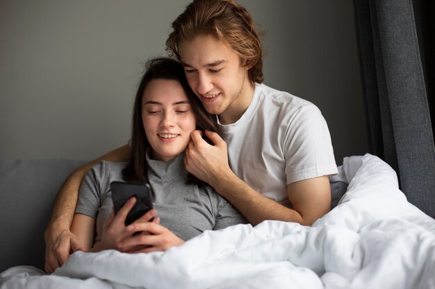 Abrazos pareja mirando el teléfono inteligente en la cama