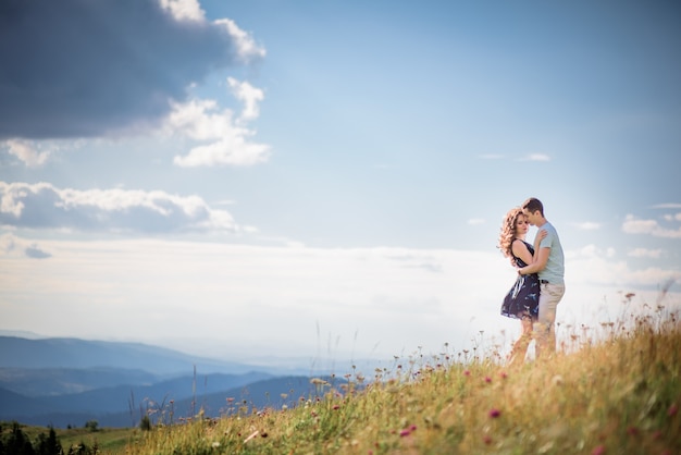 Abrazos tiernos de una pareja de pie en una colina verde antes de un paisaje precioso