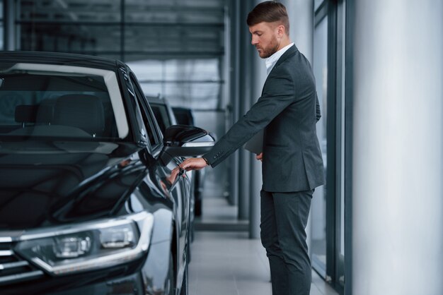 Abriendo la puerta. Empresario barbudo con estilo moderno en el salón del automóvil