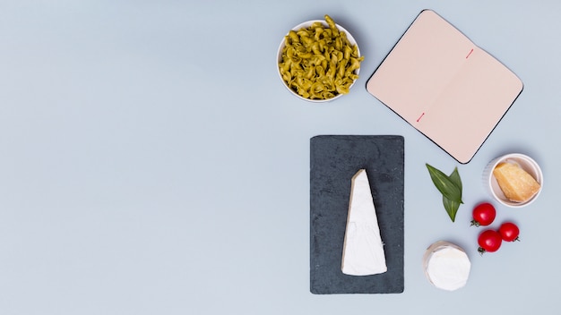 Abrir libro en blanco y pasta sin cocer con ingrediente sobre fondo gris