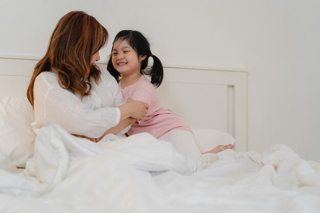 Abuela asiática relajarse en casa. Los chinos mayores, la abuela feliz se relajan con la muchacha joven de la nieta que disfruta cerca de su sorpresa de los ojos que juega junto que miente en cama en dormitorio en casa en el concepto de la noche.