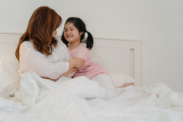 Abuela asiática relajarse en casa. Los chinos mayores, la abuela feliz se relajan con la muchacha joven de la nieta que disfruta cerca de su sorpresa de los ojos que juega junto que miente en cama en dormitorio en casa en el concepto de la noche.