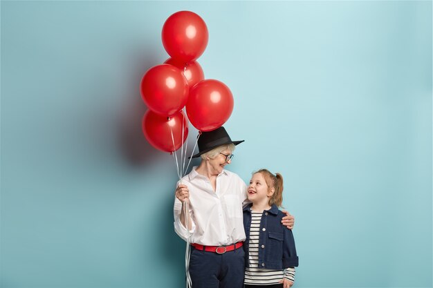 La abuela cariñosa feliz sostiene un montón de globos rojos, felicita a la nieta con el cumpleaños