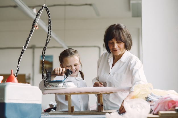 Abuela con nieta pequeña plancha ropa en la fábrica.