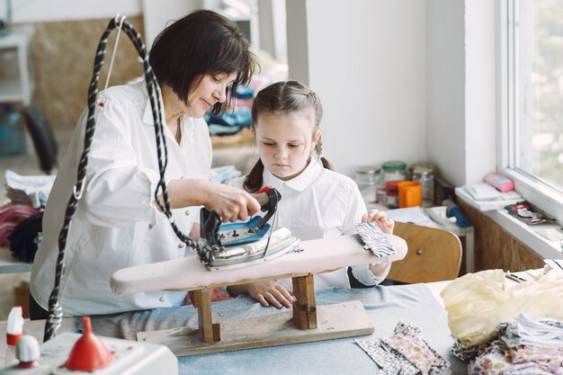 Abuela con nieta pequeña plancha ropa en la fábrica.