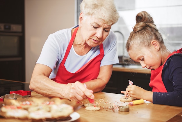 Abuela con niña horneando y decorando galletas juntos