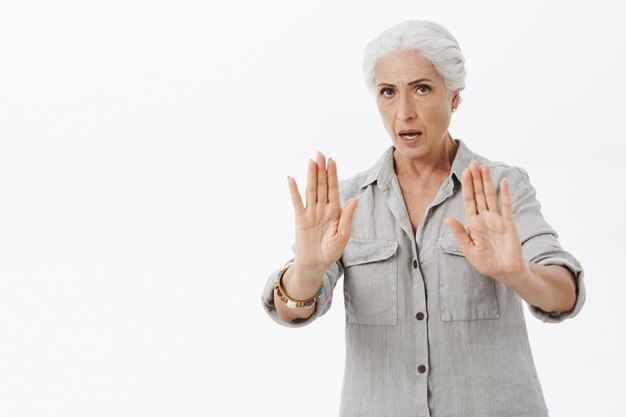 Abuela seriamente preocupada levantando las manos en gesto de parada, dígale que se calme