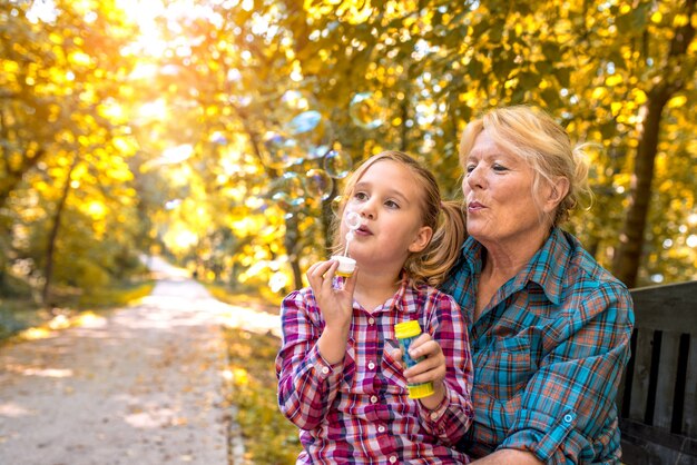 Abuela y su linda nieta soplando burbujas en un parque en un día soleado