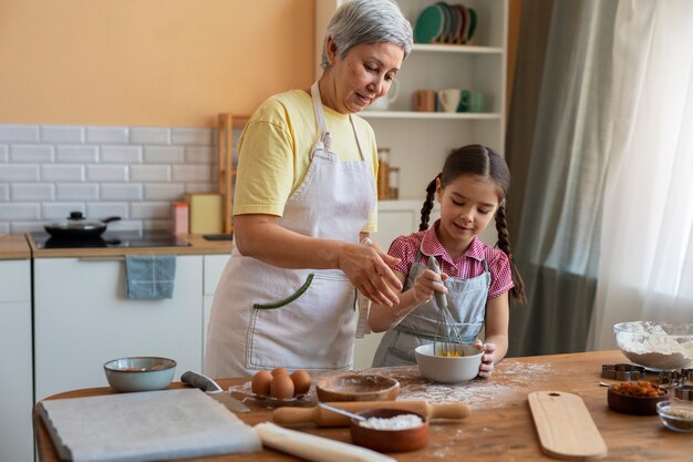 Abuela de tiro medio y niña cocinando juntas