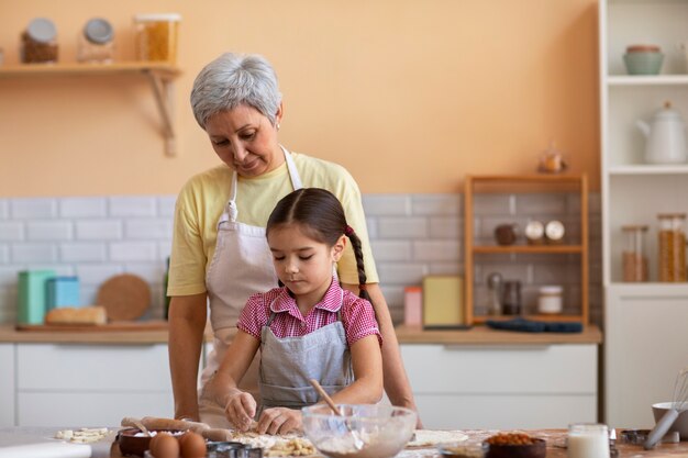 Abuela de tiro medio y niña cocinando juntas