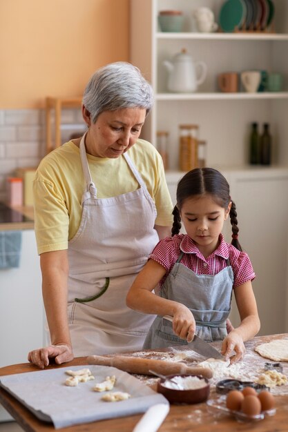 Abuela de tiro medio y niña cocinando juntas