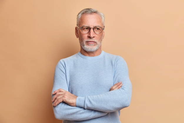 El abuelo de cabello gris y pensativo mantiene los brazos cruzados y mira hacia otro lado pensativamente reflexiona sobre algo importante vestido con un suéter informal y está absorto en sus pensamientos se siente solo como si vive solo