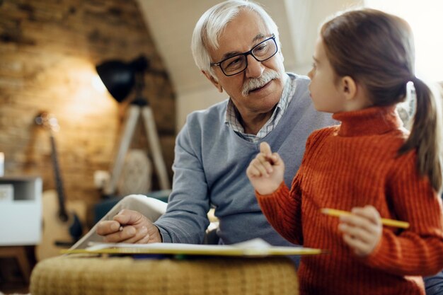 Abuelo mayor hablando con nieta mientras colorea juntos en casa