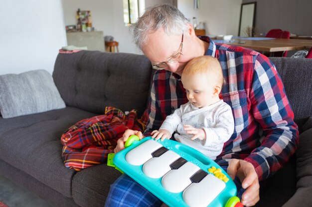 Abuelo de pelo gris sentado en el sofá y jugando con el bebé