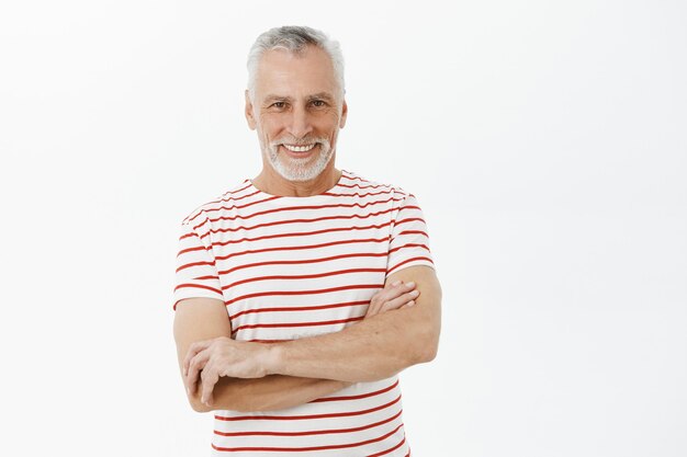 Abuelo sonriente confiado cruza el pecho de brazos y parece feliz