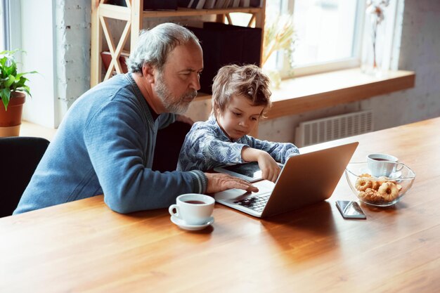 Abuelo y su nieto pasan tiempo aislados en casa, divirtiéndose, cuidando plantas, regando