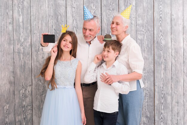 Abuelo tomando selfie en su teléfono móvil con su esposa y nietos usando accesorios