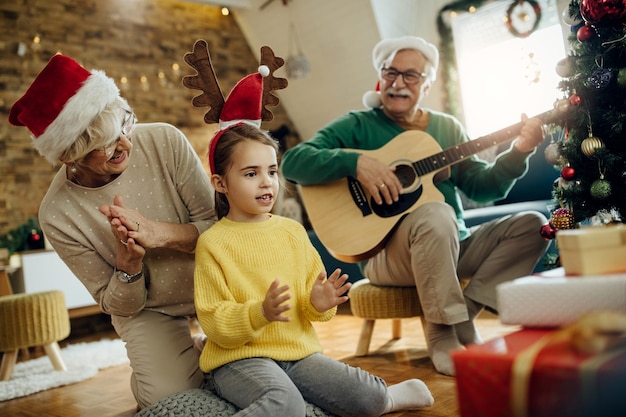 Abuelos alegres con nieta divirtiéndose en Navidad en casa