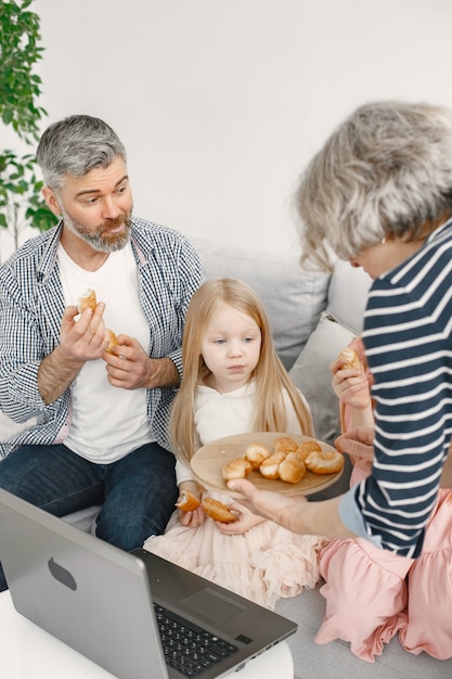 Los abuelos pasan tiempo con sus nietos. Abuela sirviendo bocadillos para niñas. Están sentados en el sofá con el portátil sobre la mesa.