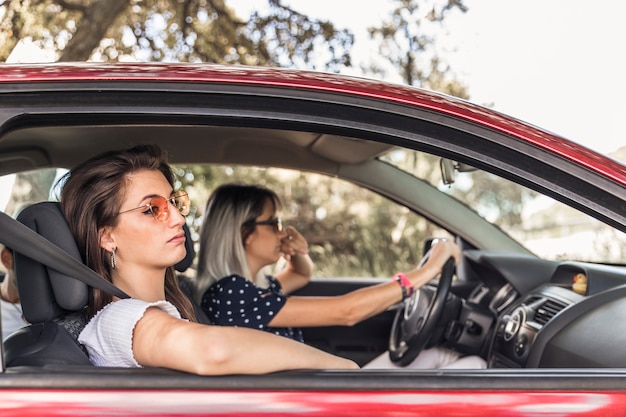 Aburrida mujer joven que viaja en coche moderno con su amigo