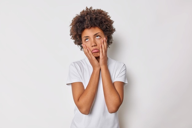 Aburrida mujer rizada disgustada hace que las palmas de las manos se vean con expresión cansada y desinteresada por encima de los ojos de rollos no quiere escucharlo vestido con una camiseta básica casual aislada sobre fondo blanco