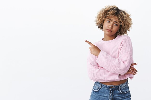 Aburrido, tan pasado de moda. Decepcionada, triste y molesta linda chica afroamericana con nariz perforada y corte de pelo rubio afro inclinando la cabeza con el ceño fruncido, enfurruñado y disgustado, apuntando a la esquina superior izquierda