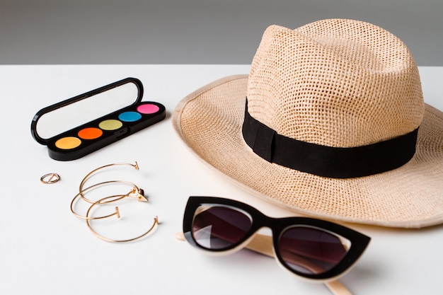 Accesorios cosméticos decorativos gafas de sol y sombrero en mesa blanca.