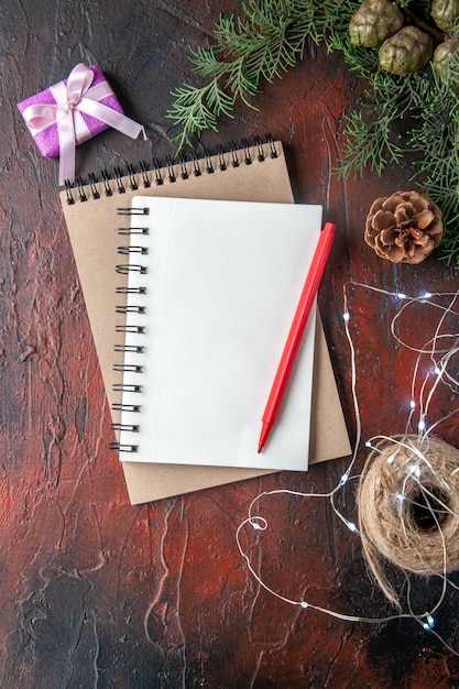 Accesorios de decoración de ramas de abeto y regalo y cuadernos con lápiz sobre fondo oscuro