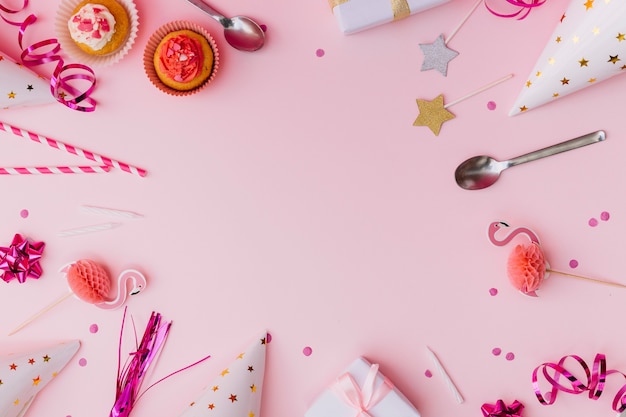 Accesorios de fiesta con cupcake y cuchara sobre el fondo rosa.