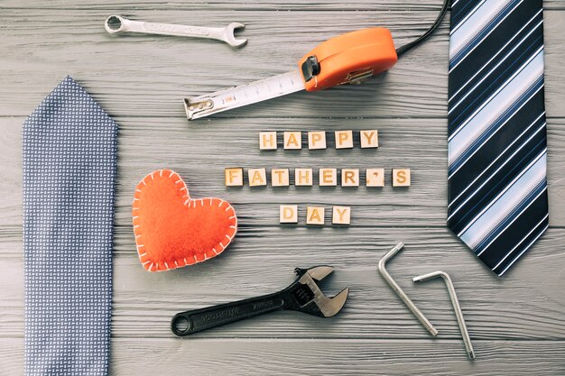 Accesorios masculinos cerca de instrumentos y felices palabras del día del padre con corazón