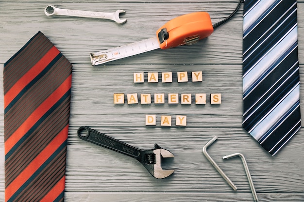 Accesorios masculinos cerca de instrumentos y felices palabras del día del padre con corbatas.