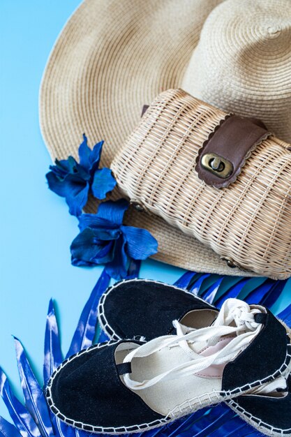 Accesorios de verano, zapatos y sombrero con bolsa sobre fondo azul.