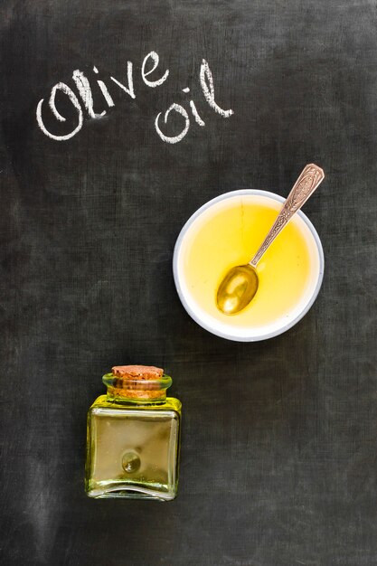 Aceite de oliva en tazón y botella cerrado con corcho en pizarra