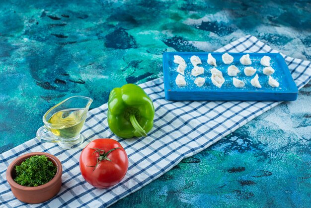 Aceite y verduras junto a los ravioles turcos en una tabla sobre el paño de cocina, sobre la mesa azul.