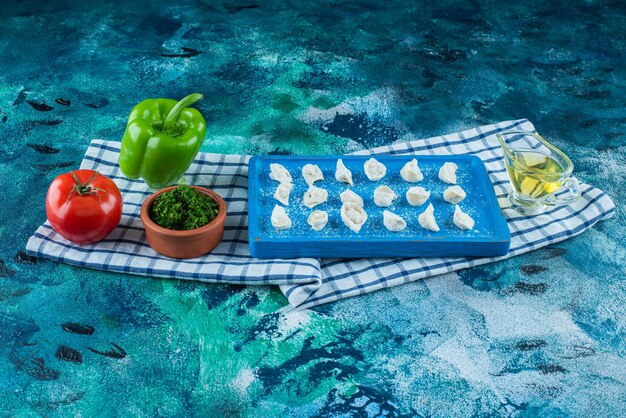 Aceite y verduras junto a los ravioles turcos en una tabla sobre el paño de cocina, sobre la mesa azul.