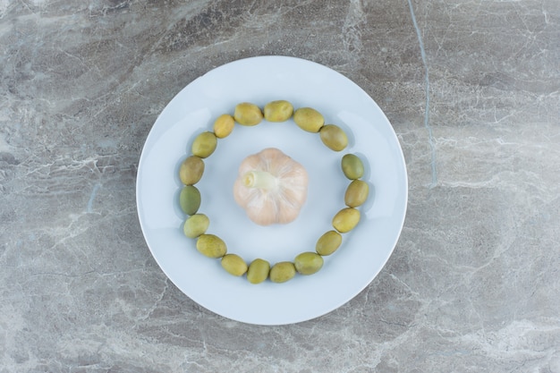 Aceitunas marinadas alrededor de ajo enlatado en un plato blanco.