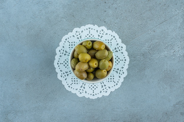 Aceitunas verdes en un recipiente sobre una montaña, sobre la mesa de mármol.