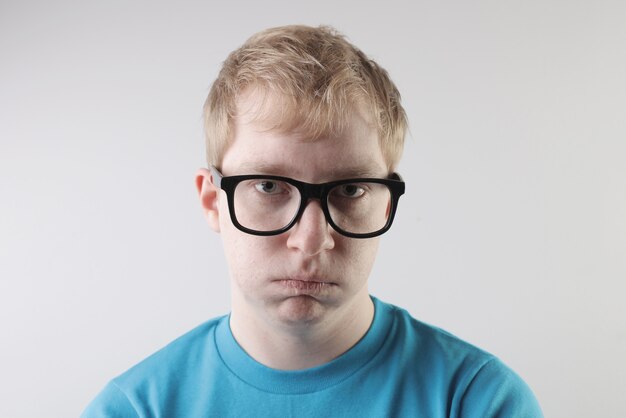 Acercamiento de un hombre caucásico con una camiseta azul y anteojos haciendo gestos graciosos