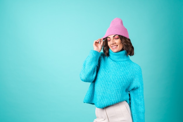 Acogedor retrato de una mujer joven con un suéter azul de punto y un sombrero rosa con maquillaje brillante